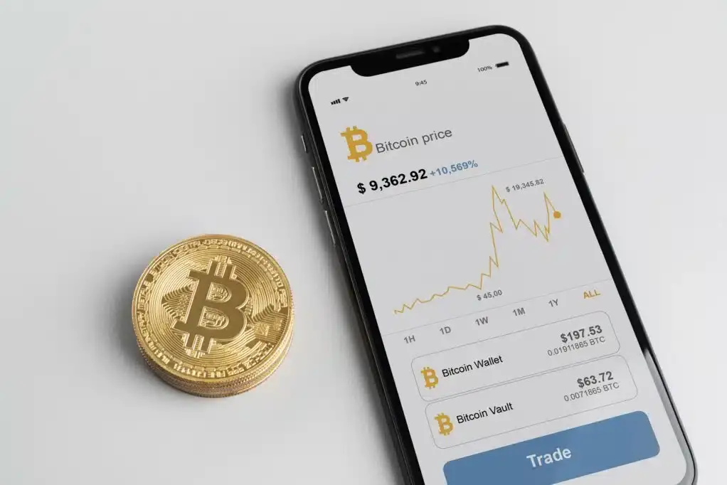 Смартфон із графіком ціни біткоїна та монета біткоїна поруч